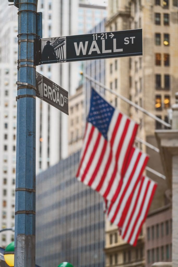 Wall Street "WALL ST" sign and broadway street over American national flags